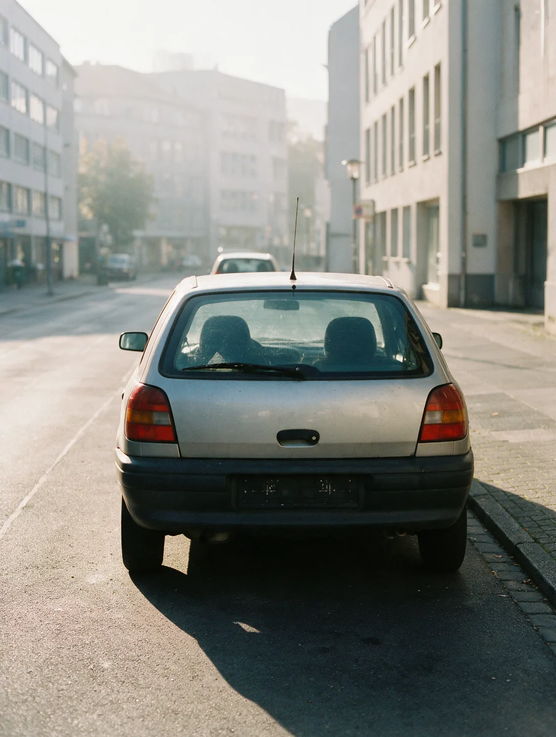 Ein parkendes Auto von hinten in einer kopfsteingepflasterten Altstadtstraße im Morgendunst.
